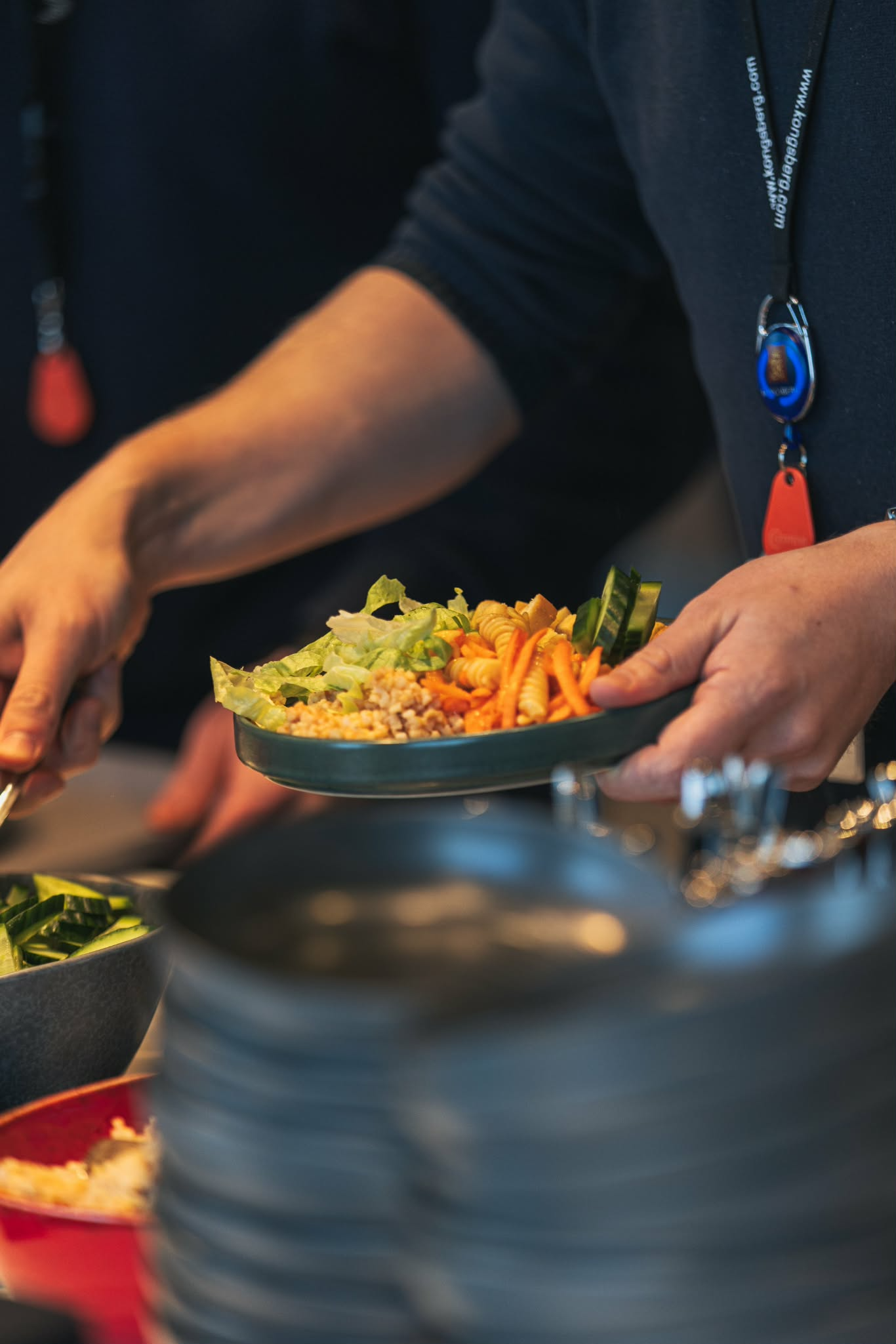 En person som serverer en tallerken med salat og grønnsaker, med tallerkener stablet i bakgrunnen.