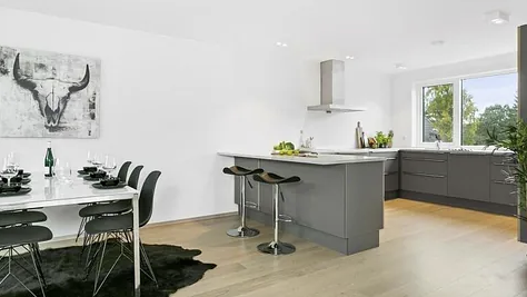 Moderne kjøkken med grå skap, spisebord med stoler og en stor vindu som slipper inn naturlig lys.