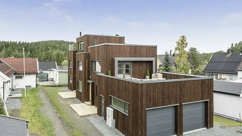 Moderne trehus med garasje og terrasse, omgitt av grønt landskap og nabolag.