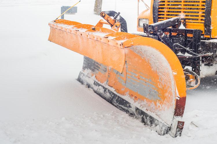 Snøplog i oransje farge står klar til å rydde snø fra veien i vinterlandskap.