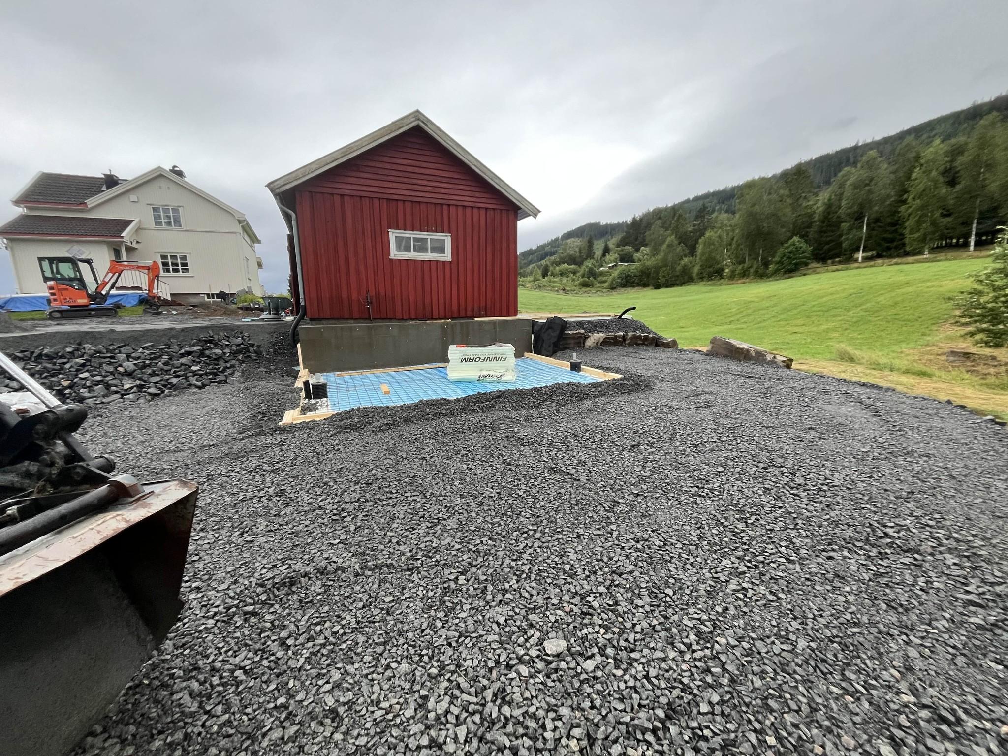 Rødt hus på en gruslagt tomt med grønt landskap i bakgrunnen og en blå bassengramme.