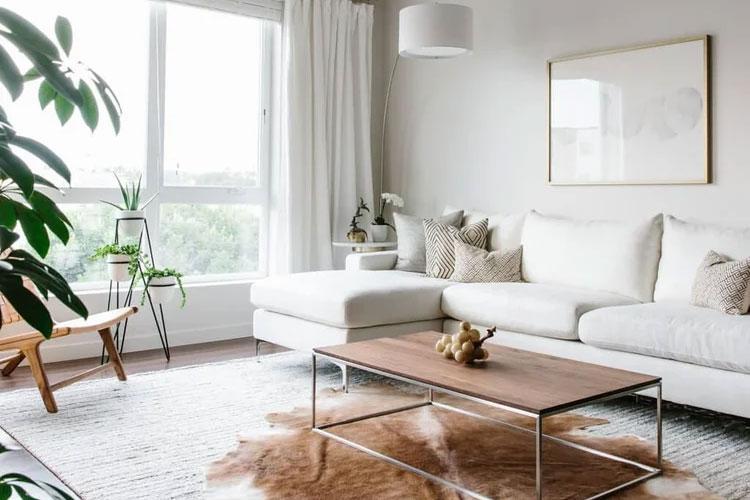 Lyst stue med hvit sofa, trekaffebord, plante og moderne dekor på veggen.
