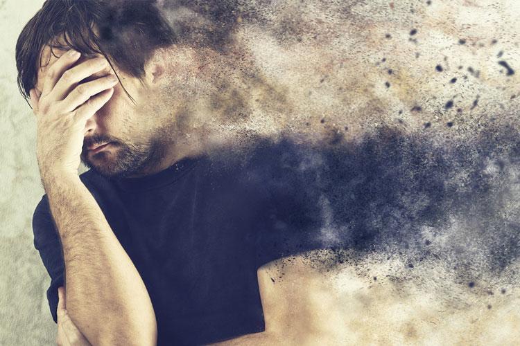 En mann holder hodet i hånden, omgitt av en sky av støv og partikler som symboliserer stress og angst.