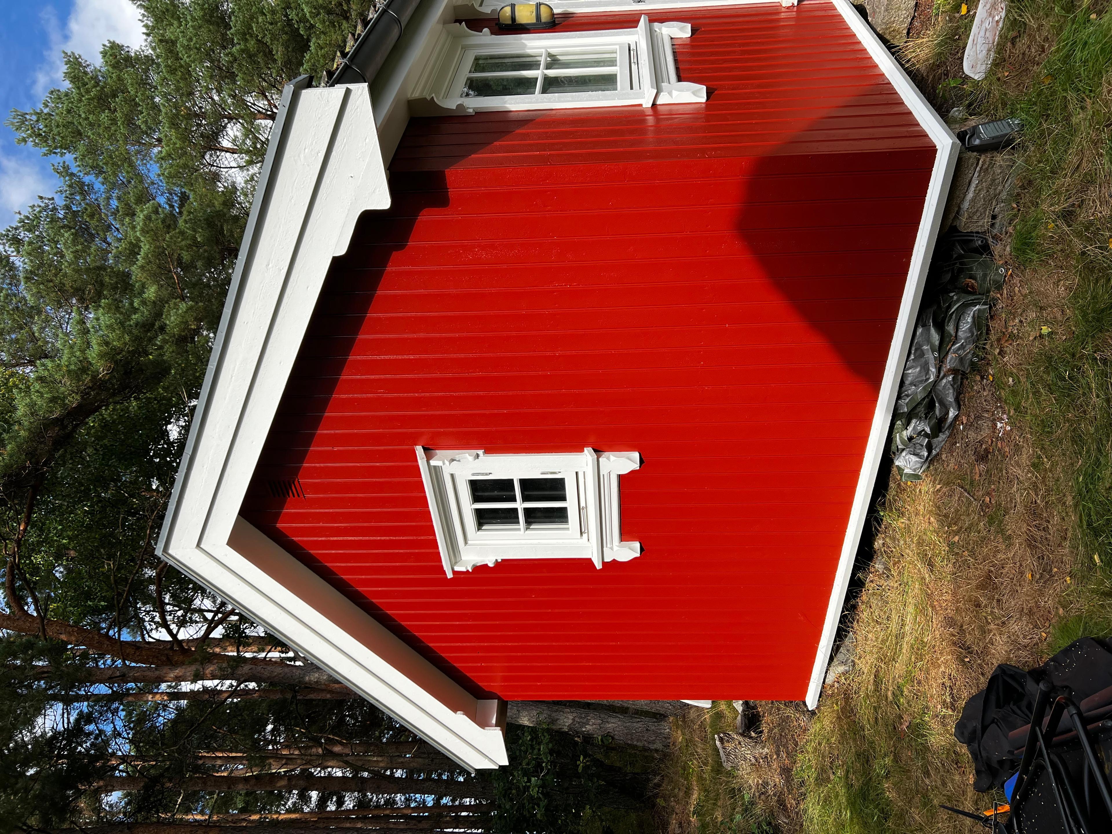 Rødt hus med hvite vinduer og skråtak, omringet av trær og gress.