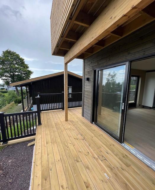 Utsikt fra en tredekk med moderne hus i bakgrunnen, omkranset av grønt landskap.