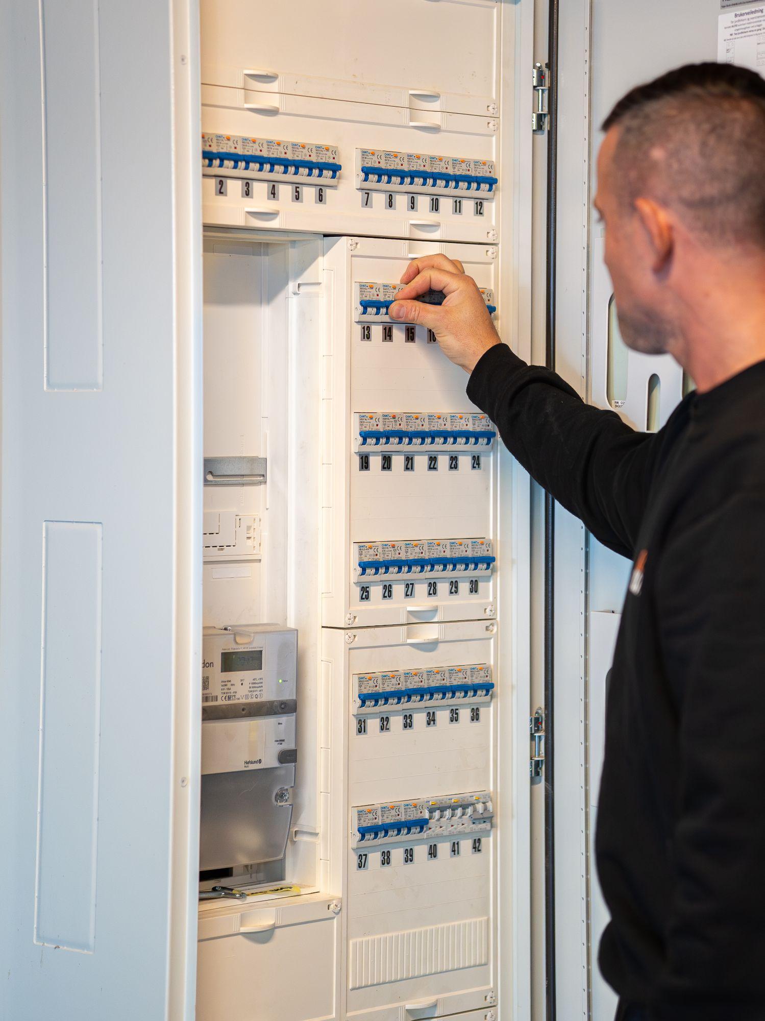 En elektriker justerer sikringene i et elektrisk skap med flere sikringsbrytere.