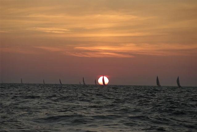 Solnedgang over havet med seilbåter i horisonten, skaper en vakker og fredelig atmosfære.