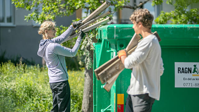 To personer som kaster hageavfall i en grønn søppeldunk på en solfylt dag.