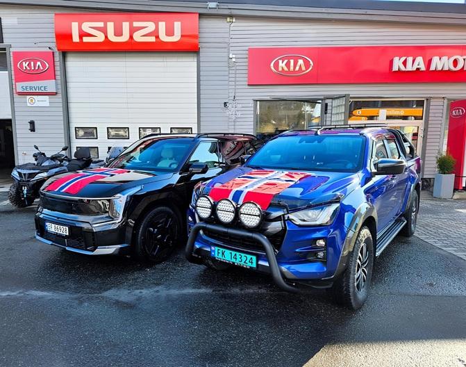 To biler parkert foran en bilforhandler, en svart SUV med striper og en blå SUV med lysbøyle.