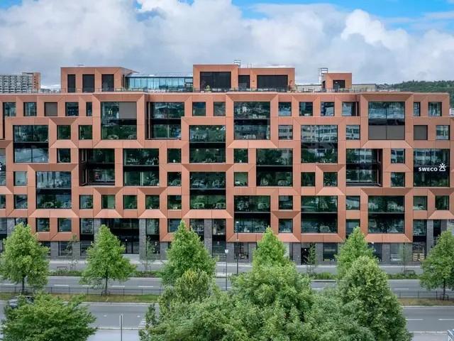 Moderne leilighetsbygg med unike vindusformer og grønne trær foran, under en skyet himmel.