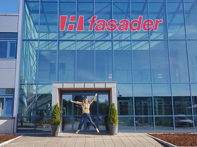 En person står foran en moderne bygning med glassfasade og et stort skilt med teksten "H fasader".