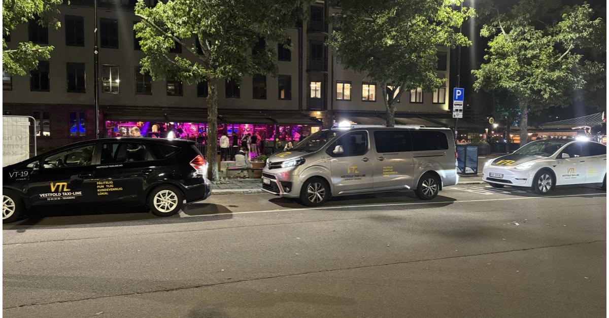 En gate med flere biler parkert om natten, med en livlig bar i bakgrunnen og grønne trær langs fortauet.