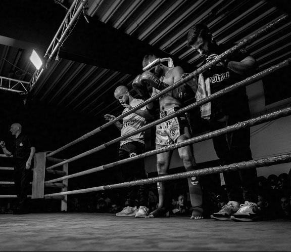 En muay thai-utøver står i ringen med trenere som gir støtte før kampen.