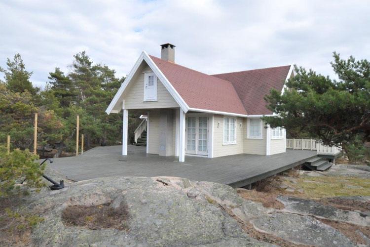 En koselig hytte med rød tak og terrasse, omringet av steiner og trær i et naturskjønt område.