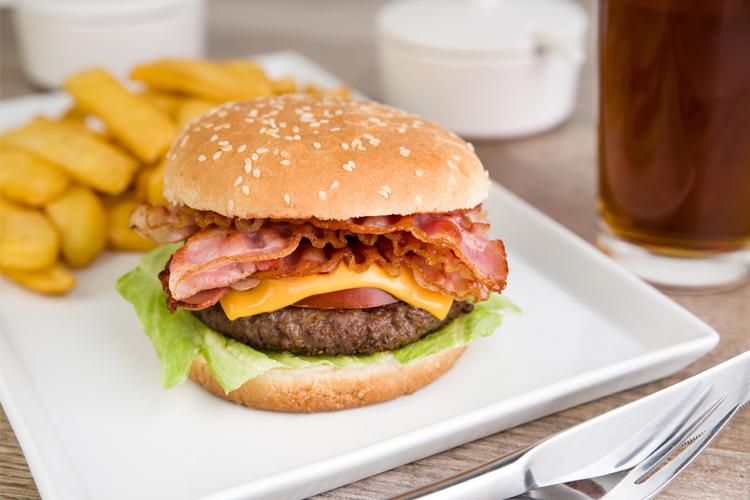En saftig hamburger med bacon, cheddarost, salat og tomat, servert med pommes frites og en drink.