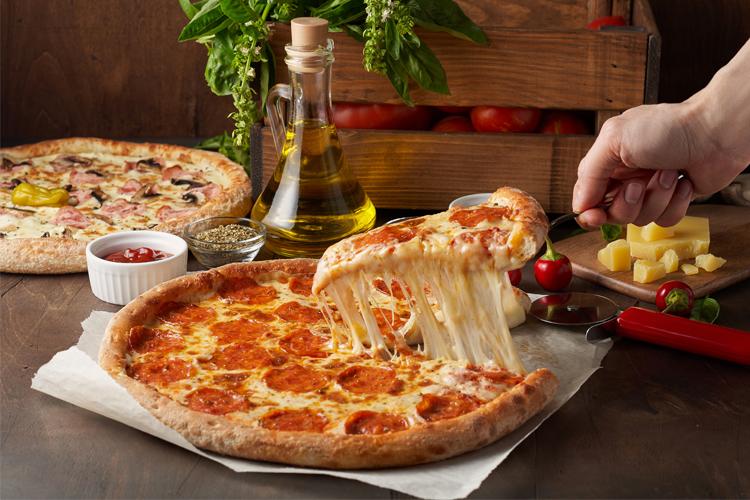 En nybakt pizza med pepperoni og smeltet ost, servert med tomatsaus og olivenolje, i en koselig kjøkkeninnstilling.