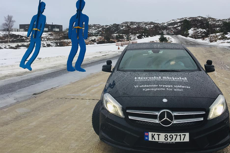 En svart Mercedes med registreringsnummer KT 89717 står på en vei med snø, med to blå figurer i bakgrunnen.