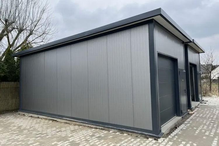Moderne grå garasje med to porter, plassert på en steinlagt gårdsplass under en overskyet himmel.