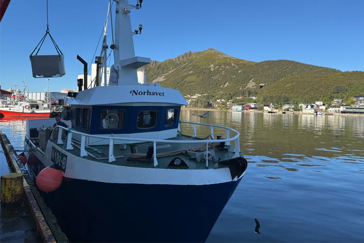 Fiskebåt ved kai med navnet "Northern" og fjell i bakgrunnen på en klar dag.