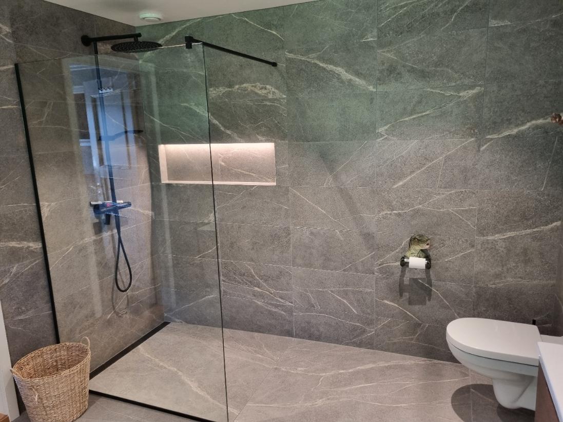 Moderne baderom med dusjhjørne, glassdør, toalett og grå marmorvegger.