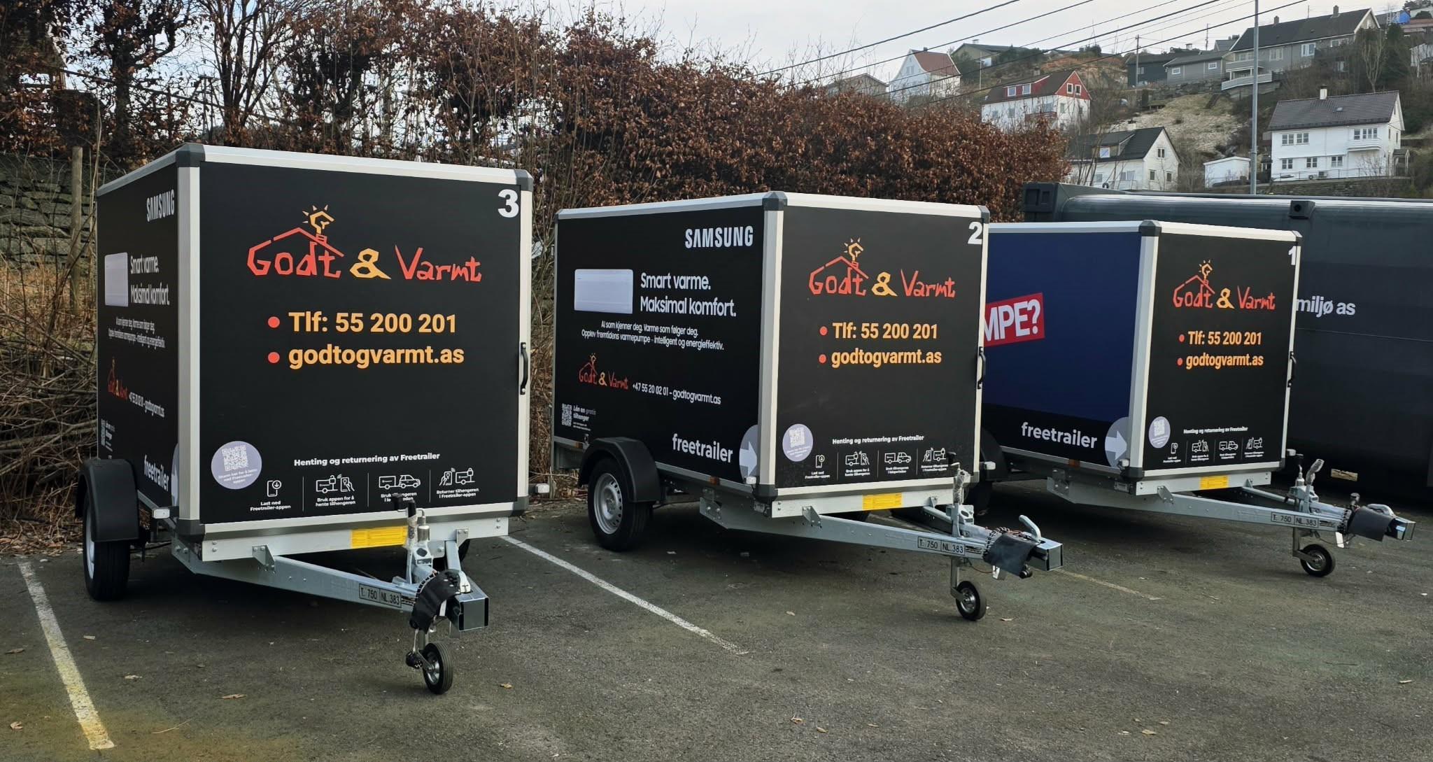 Tre tilhengere med reklame for "Godt & Vondt" parkert på en parkeringsplass.