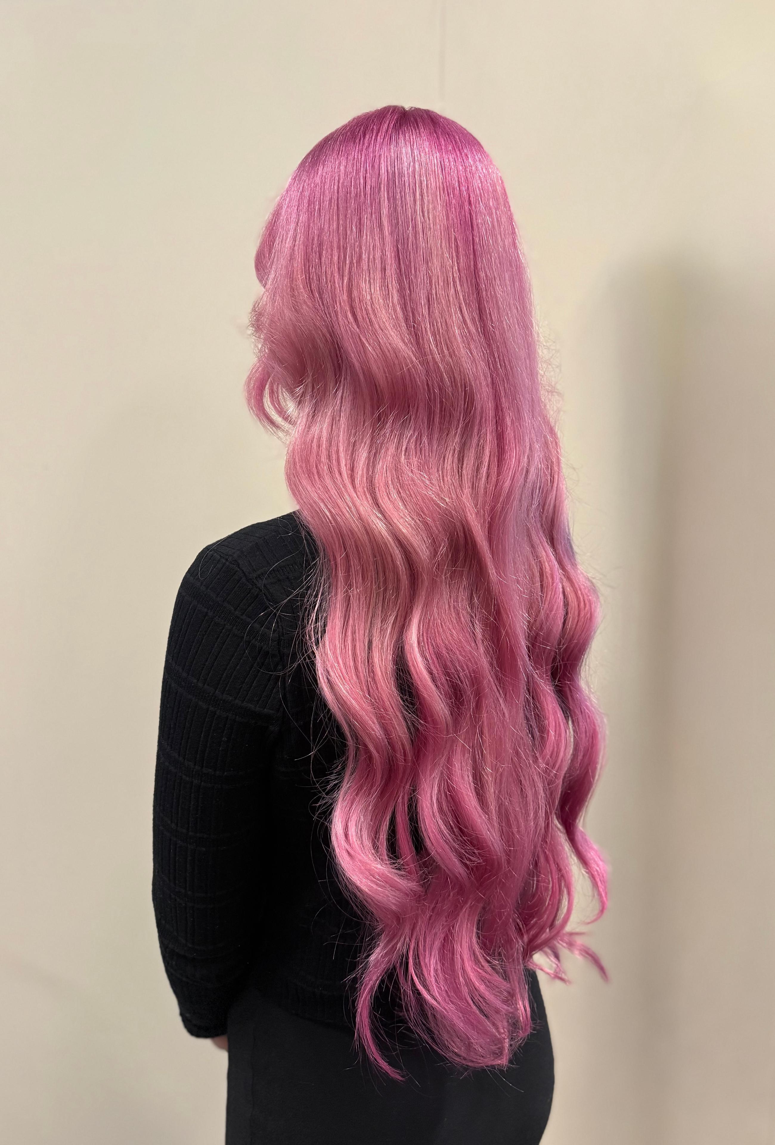 Langt, bølgete rosa hår på en kvinne sett bakfra, iført en svart genser.
