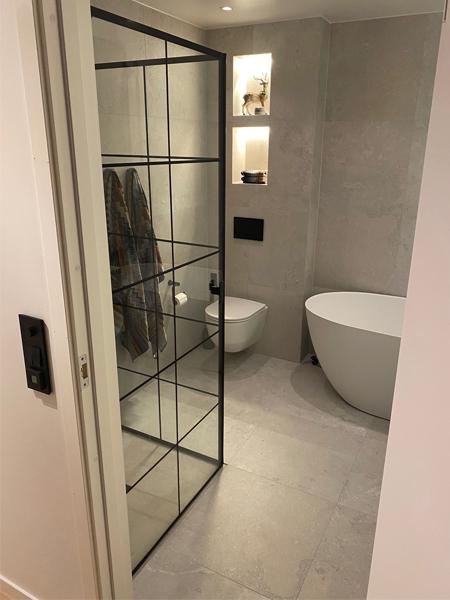 Moderne bad med badekar, toalett og glassvegg som skiller rommet fra gangen.