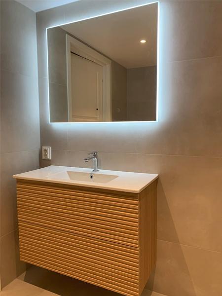 Moderne baderom med en lysende speil over en trekommode med vask og minimalistisk design.