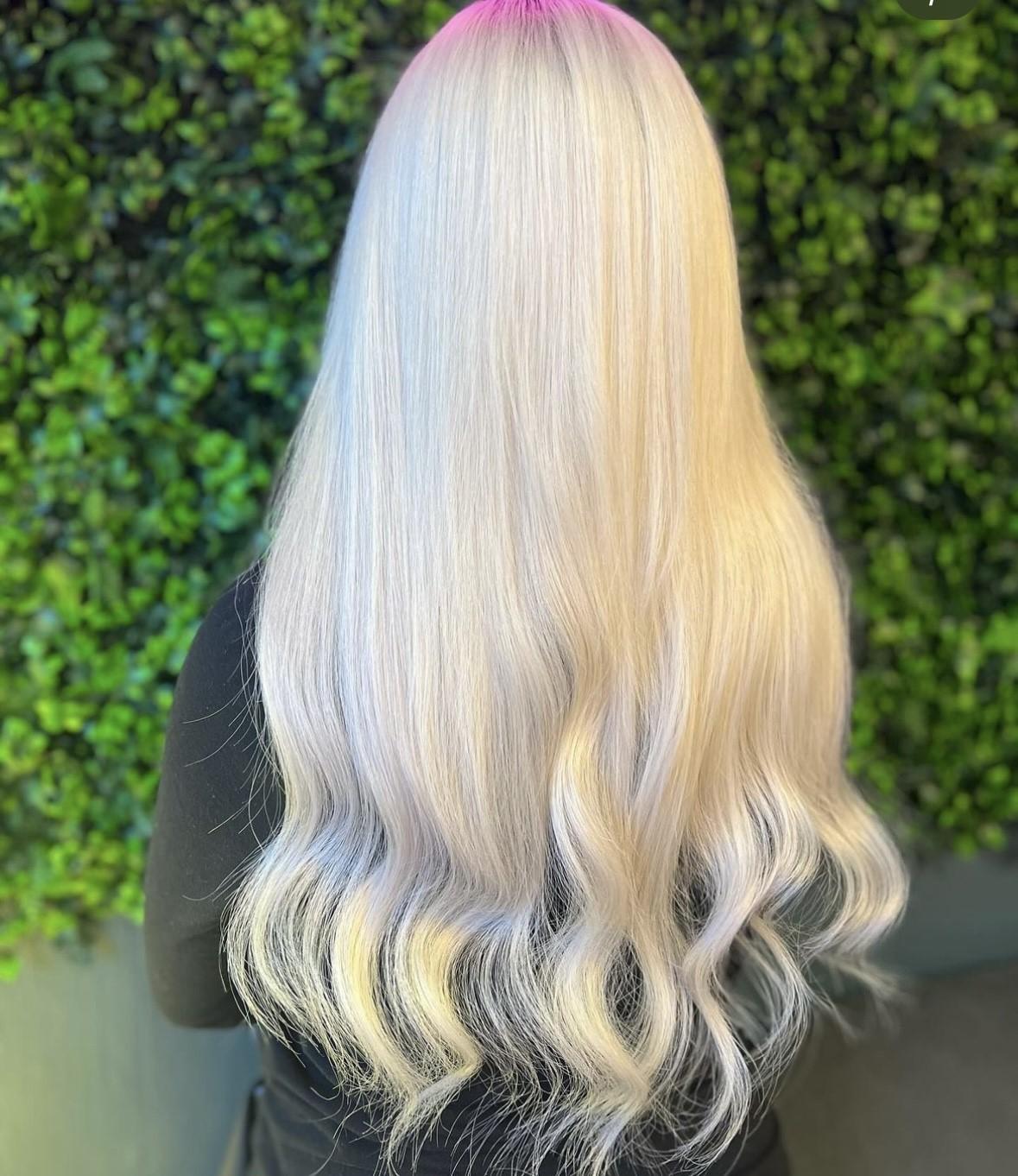 Langt, bølgete hår med lys blond farge og rosa striper, sett bakfra mot en grønn bakgrunn.