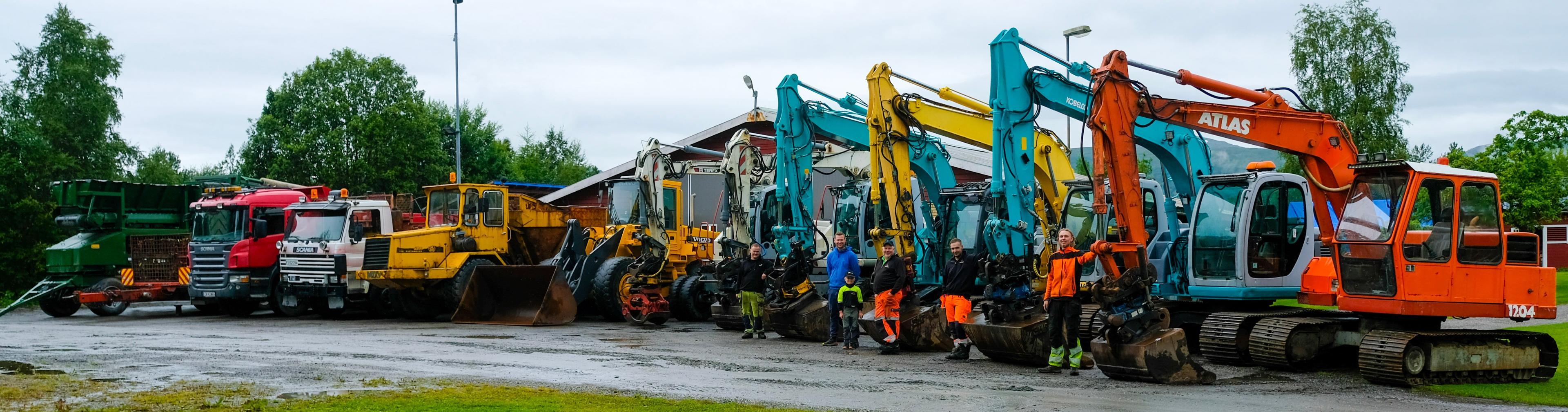 En rekke fargerike gravemaskiner og lastebiler parkert på en grusvei med trær i bakgrunnen.
