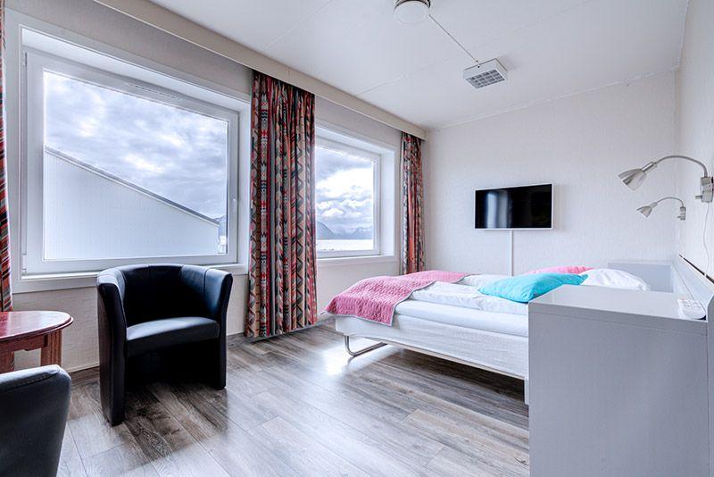 Moderne soverom med dobbeltseng, stoler, TV og store vinduer som slipper inn naturlig lys.