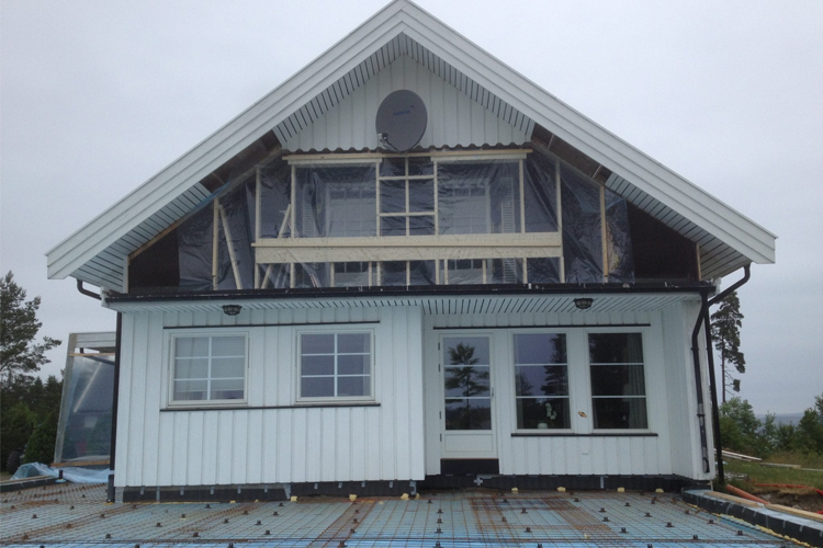 Moderne, hvitt hus med skråtak og store vinduer, under bygging med plastdeksel og takpapp.