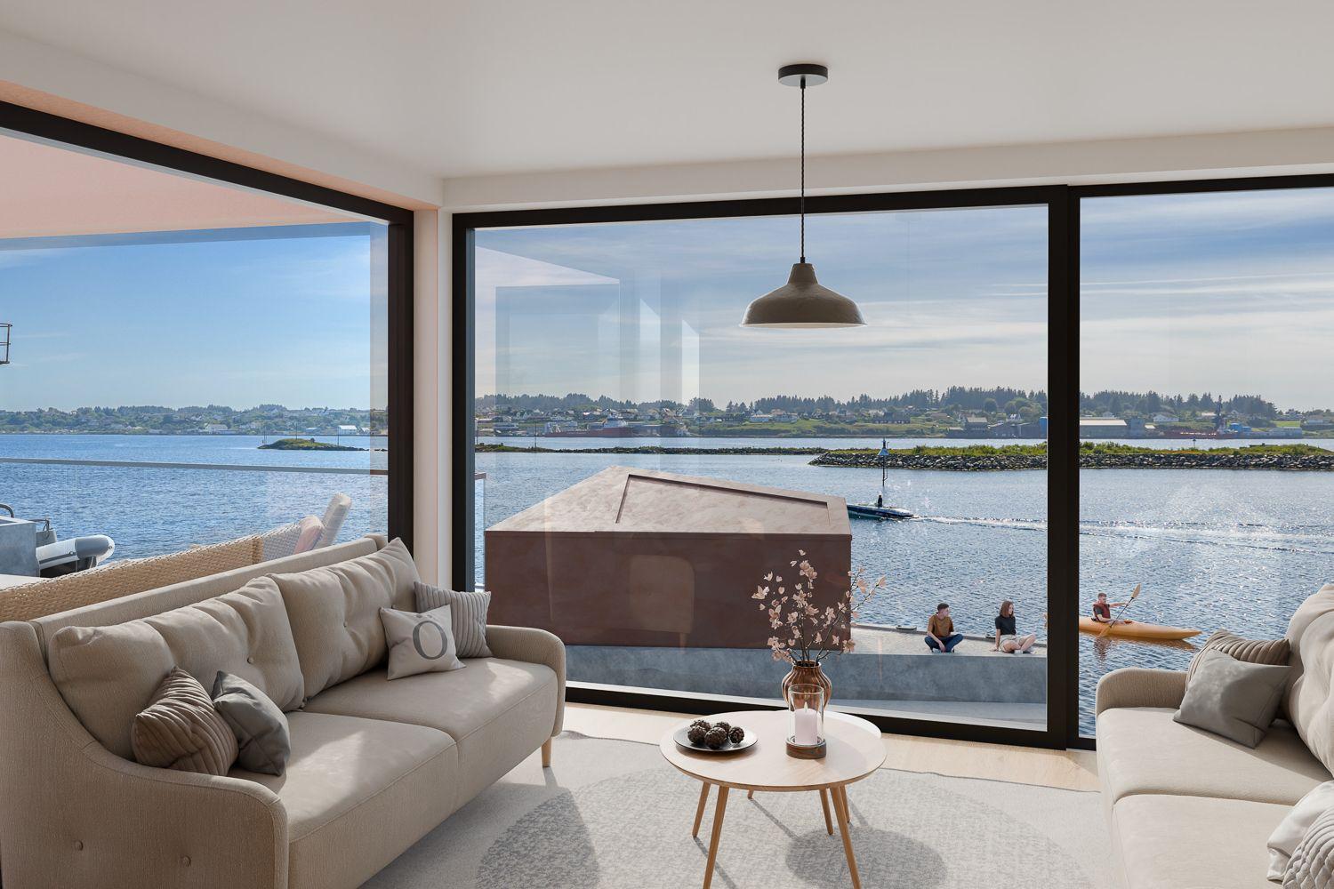 Moderne stue med utsikt over vannet, sofaer, bord og båter i bakgrunnen. Solfylt dag med klar himmel.