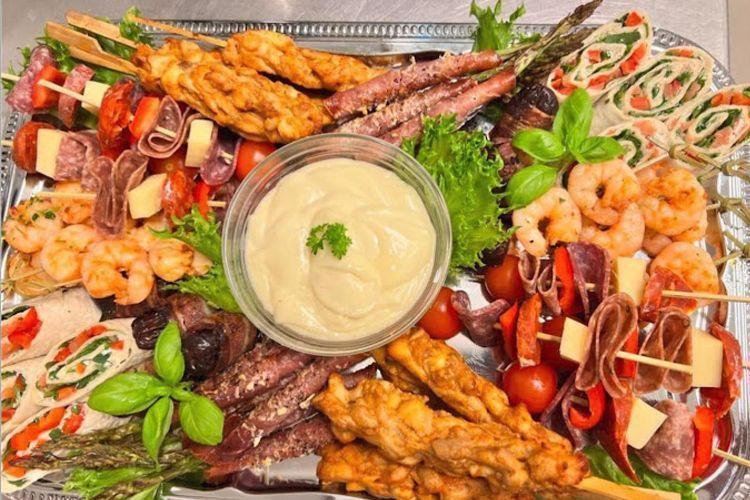 Et fat med variert tapas, inkludert reker, spekemat, grønnsaker, og en kremet dipp i midten.