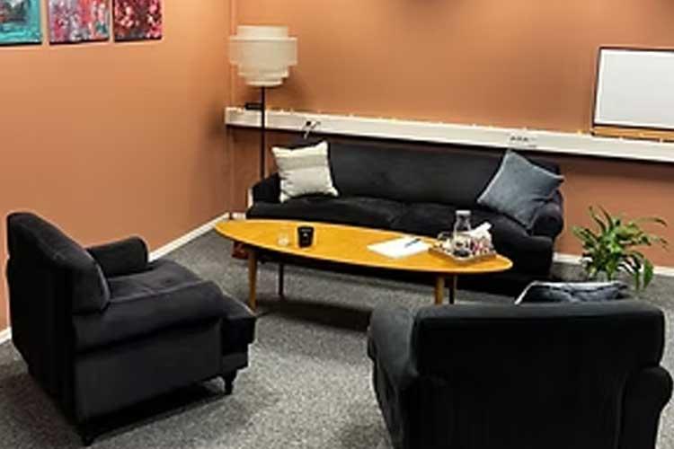 Et koselig rom med en svart sofa, to stoler, et rundt bord og en plante, med kunstverk på veggen.