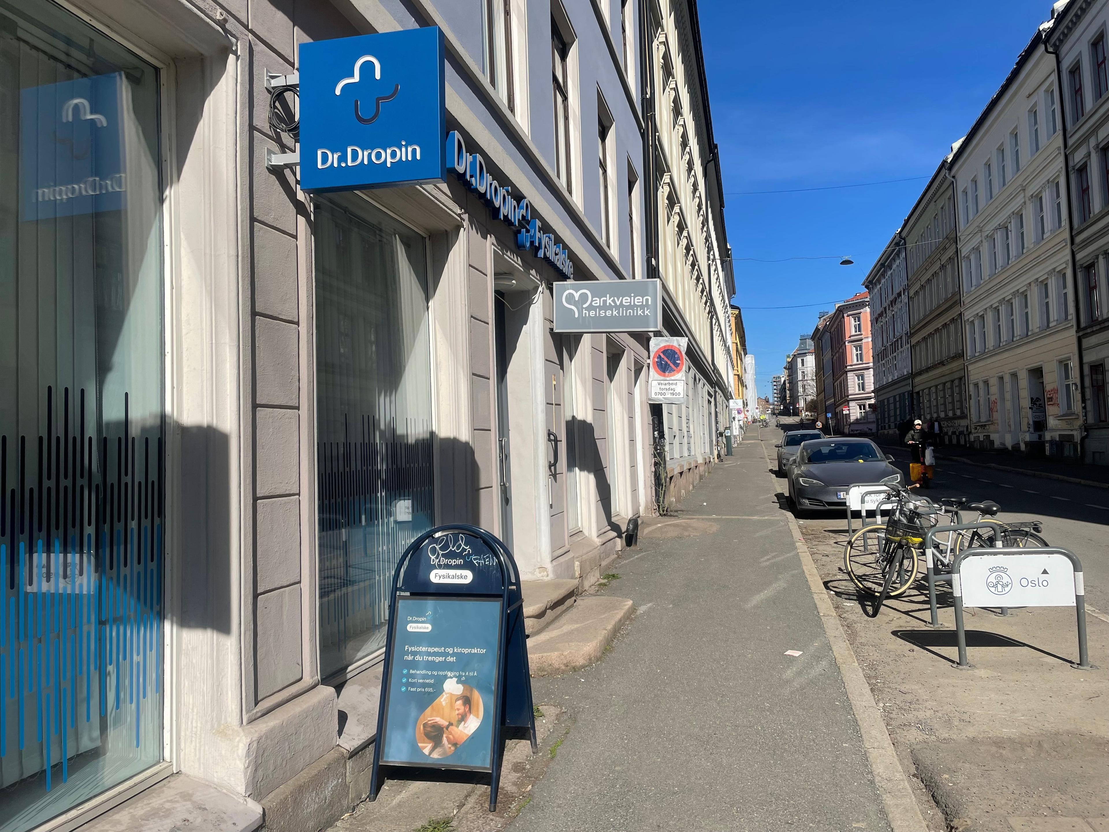 Gatebilde med Dr.Dropin-skjold og andre butikker langs fortauet på en solfylt dag.
