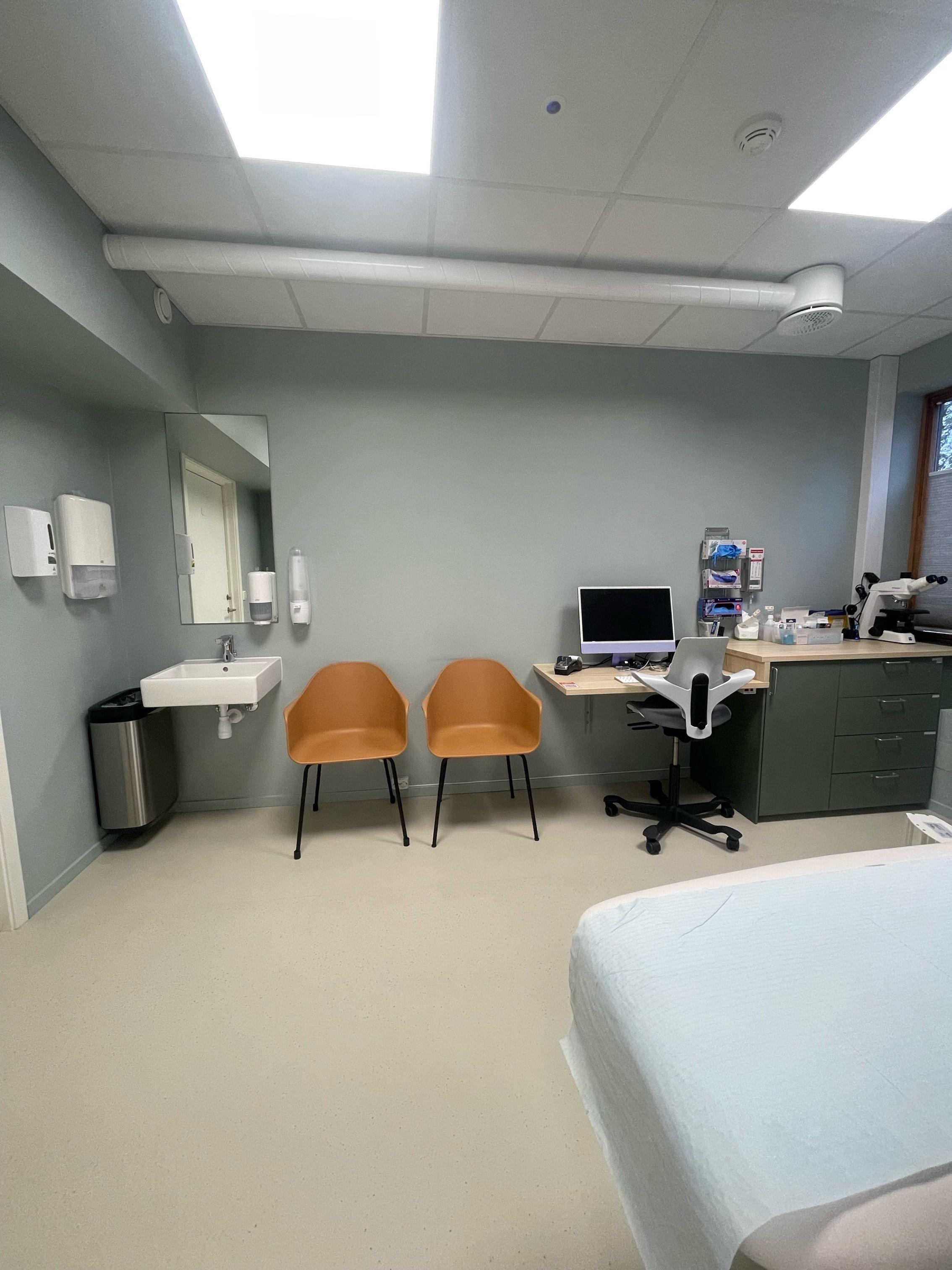 Moderne legekontor med to stoler, datamaskin, vask og medisinsk utstyr på en arbeidsbenk.