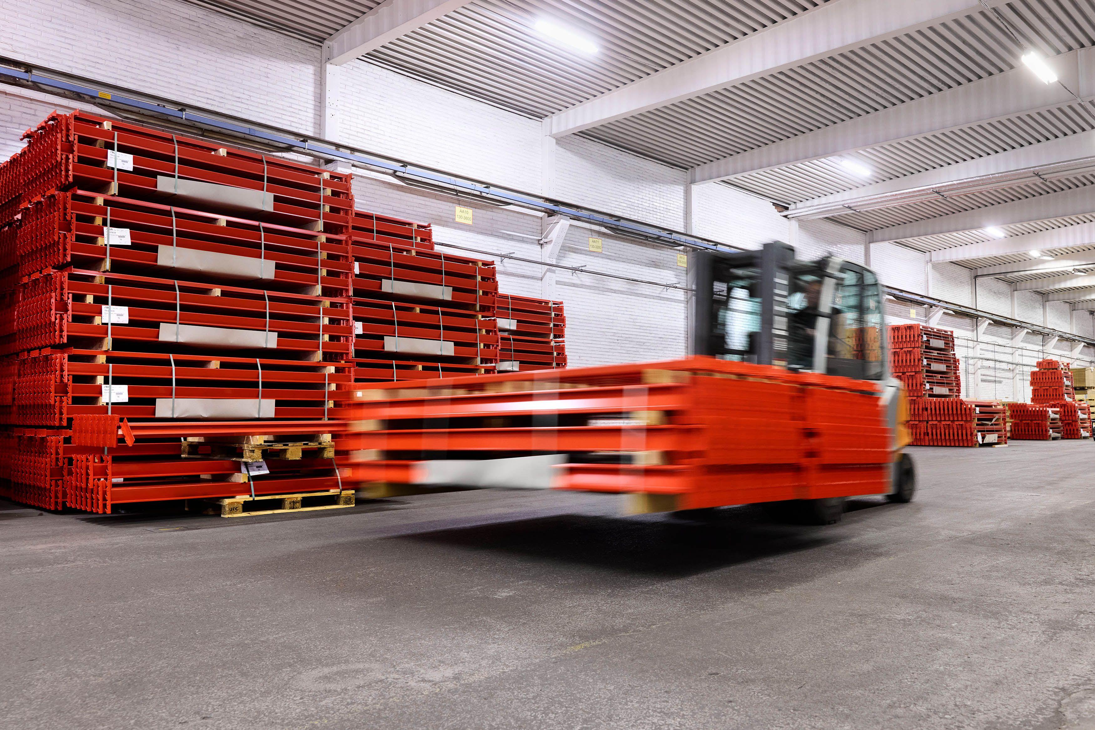 Gaffeltruck som kjører forbi stablede, røde paller i et lager.