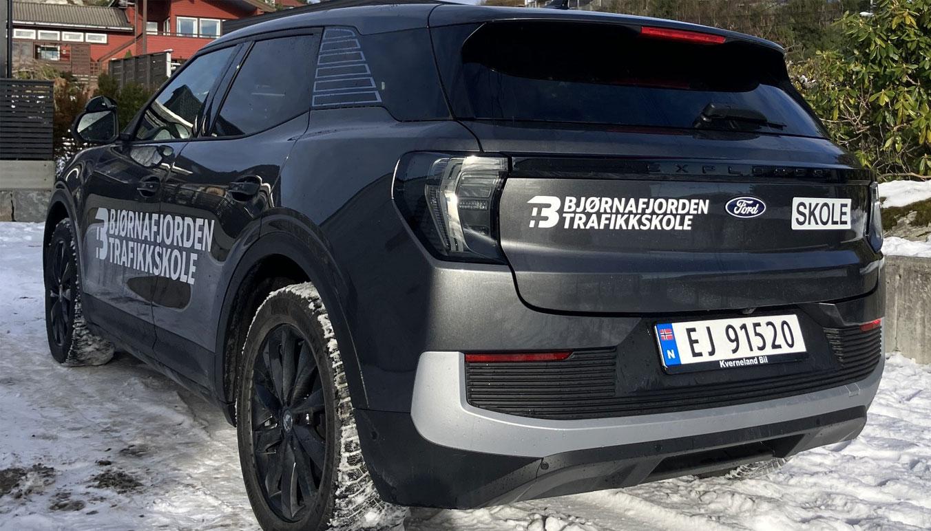 En grå bil med trafikkskole-reklame står på snøen, med registreringsnummer EJ 91520.