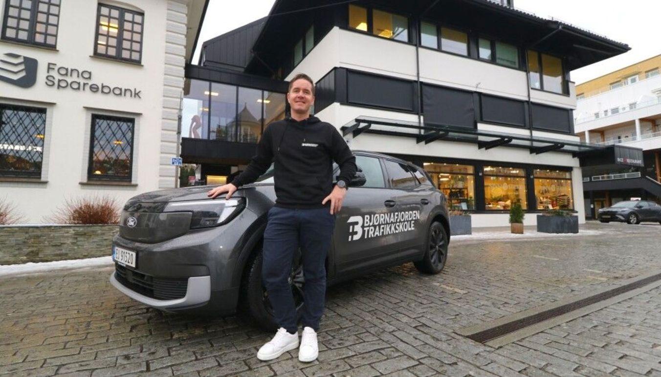 En person står ved siden av en bil med logoen til Fana Sparebank foran en bygning.