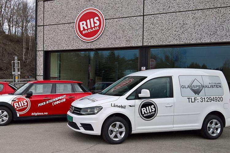 To biler parkert foran en butikk med navnet "RIIS" på fasaden.