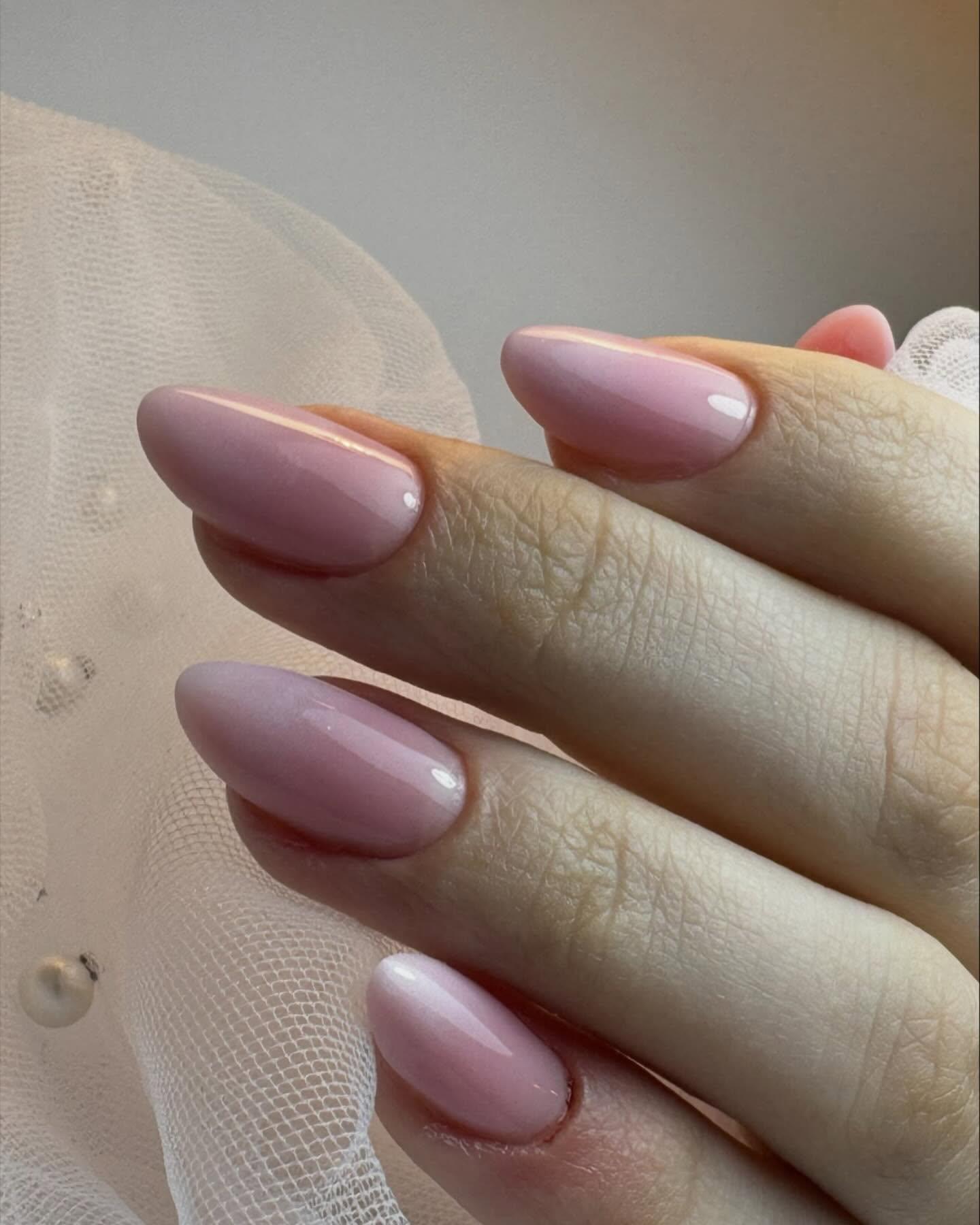 Hånd med lange, rosa negler som har en glatt og skinnende overflate, mot en lys bakgrunn.