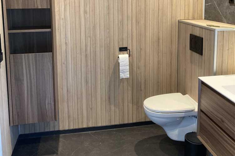 Moderne bad med trepanel, toalett, servant og oppbevaringsskap.