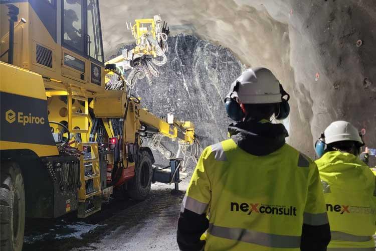 Arbeidere i sikkerhetsutstyr observerer en tunnelboremaskin i en underjordisk tunnel.