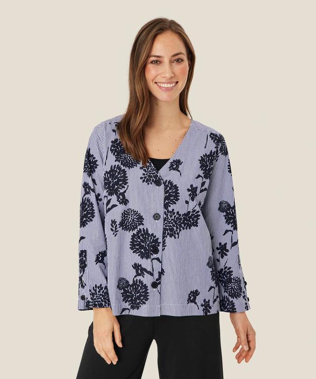 Dame i bluse med blomster- og stripemønster, smilende mot kameraet, med lys bakgrunn.