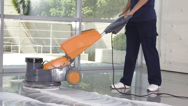 En person bruker en gulvsliper på et skinnende gulv i et moderne rom.