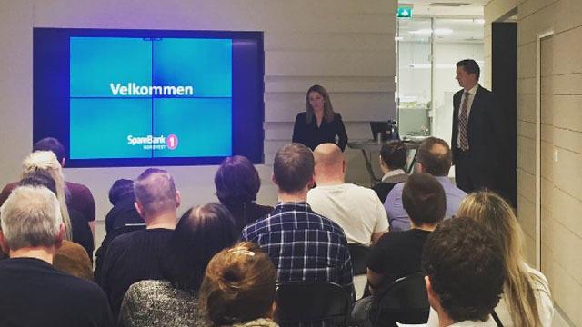 En gruppe mennesker sitter i et rom og ser på en presentasjon med teksten "Velkommen" på skjermen.