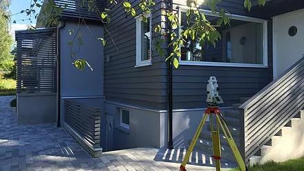 Moderne hus med grå fasade, terrasse og nivåmåler plassert på brosteinsbelagt område.
