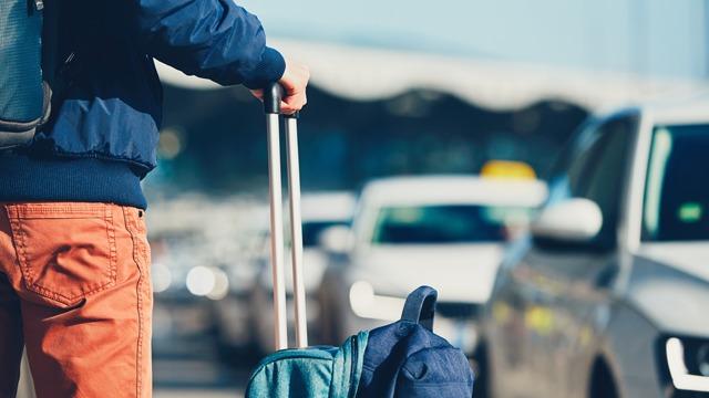 En person med en koffert står ved en taxiholdeplass på flyplassen.