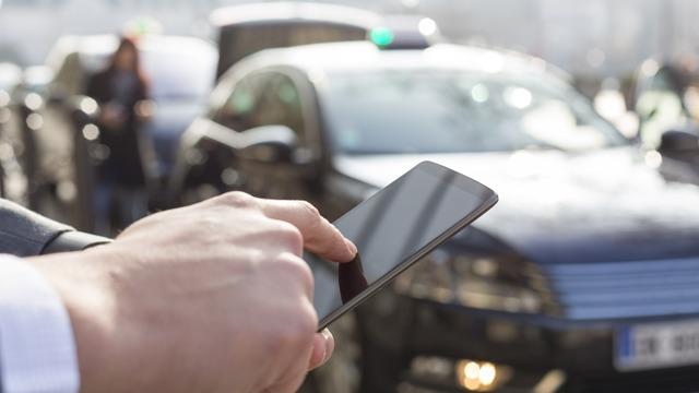 En person som bruker en smarttelefon foran en politibil i en travel gate.